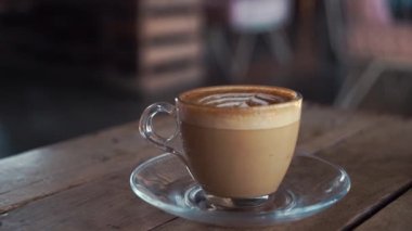 Bir kadının elindeki sıcak kahve fincanını sokak kafesindeki ahşap masanın üzerine koyarken.