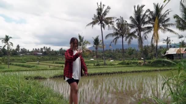 Szczęśliwa kobieta spaceruje i robi wideo i zdjęcie na telefonie w ryżu paddy korzystających wakacje zwiedzanie egzotycznych krajobrazów kulturowych podróży przez Bali indonesia — Wideo stockowe