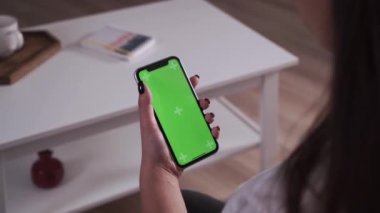 Ev soyutlanmış. Krom tuşlu yeşil ekran akıllı telefon tutan esmerin arka plan görüntüsü içeriği dokunmadan veya aşırmadan izliyor. Coronavirus Covid-19 Karantina Uzaktan eğitim veya çalışma konsepti
