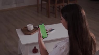 Ev soyutlanmış. Krom anahtar taşıyan esmer, yeşil ekran akıllı telefonun arkadaşıyla sohbet edişinin arka görüntüsü. Coronavirus Covid-19 Karantina Uzaktan eğitim veya çalışma konsepti