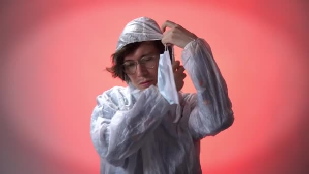 Serious man in a white protective suit on red background puts medicine mask, zips jacket, puts on a hood. Coronavirus covid-19 concept — Stock Video