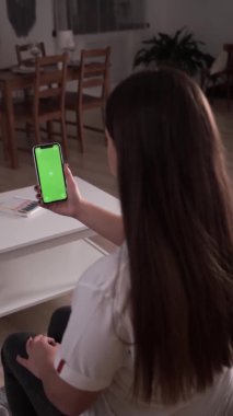Ev soyutlanmış. Krom anahtar taşıyan esmer, yeşil ekran akıllı telefonun arkadaşıyla sohbet edişinin arka görüntüsü. Coronavirus Covid-19 uzaktan eğitim ya da çalışma konsepti karantinası. Dikey video