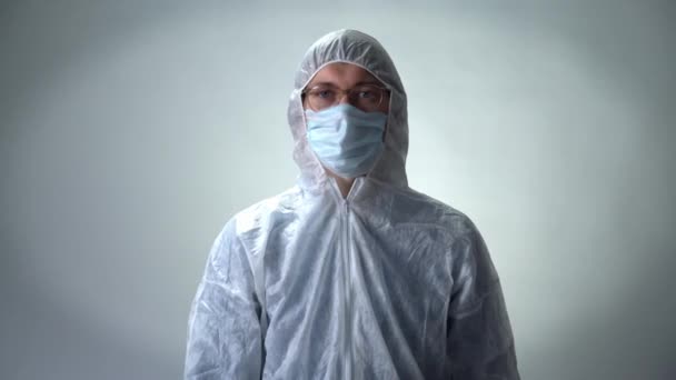 Мужчина в защитном костюме, медицинской маске и очках показывает цветы на белом фоне — стоковое видео