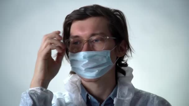 Serious man in a white protective suit on red background puts medicine mask, zips jacket, puts on a hood. Coronavirus covid-19 concept — Stock Video