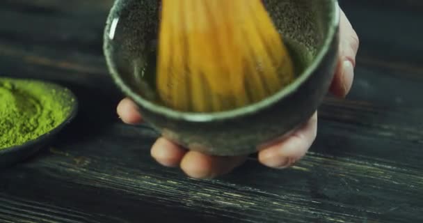 Muž připravuje zápalku zeleného čaje v misce na černém dřevěném stole. Muž přidat sirka zelený čaj prášek do misky. Matcha Organic Green Tea. Matcha Tea ceremoniál. Zavřít snímek — Stock video