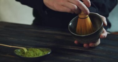 Siyah ahşap masada yeşil çay eşleşmesi hazırlayan adam. Adam kaseye kibrit yeşil çay tozu ekliyor. Kibrit Organik Yeşil Çay. Matcha Çay Töreni. Yakın çekim.