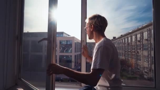 El hombre con una camiseta blanca mira por la ventana y grita durante la cuarentena. Casa aislada, cuarentena del coronavirus Covid-19 — Vídeos de Stock