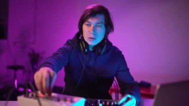 Ev kayıt stüdyosunda müzik çalan yakışıklı DJ portresi. Öğrenci yaratıcı atmosfer müziği yazmayı öğreniyor. Çevrimiçi eğitim. Ses çıkarıcı. Renkli Neon ışığı