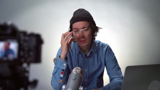 年轻的戴帽子戴眼镜的便衣男子博主看着相机在家里录音棚里记录生活方式博客，谈论分享新闻的人打视频约会在线交流 — 图库视频影像