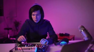 Yakışıklı DJ, stüdyo atölyesinde müzik çalıyor. Öğrenci yaratıcı atmosfer müziği yazmayı öğreniyor. Çevrimiçi eğitim. Ses çıkarıcı. Renkli Neon ışığı. Ev izole