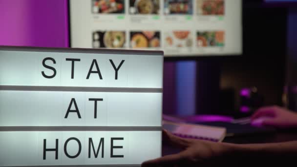 Mesajın olduğu bir tabela evde kalır, arka planda neon ışıkta çalışan bir insan. COVID-19 Coronavirus Evde KALDI Sosyal medya yazısıyla birlikte viral sosyal medya mesajını kurtardı — Stok video