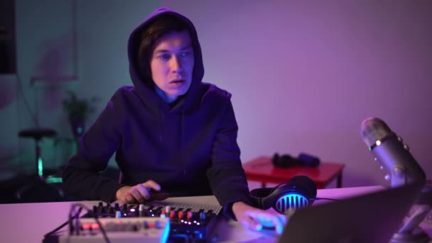 Yakışıklı DJ, stüdyo atölyesinde müzik çalıyor. Öğrenci yaratıcı atmosfer müziği yazmayı öğreniyor. Çevrimiçi eğitim. Ses çıkarıcı. Renkli Neon ışığı. Ev izole — Stok video