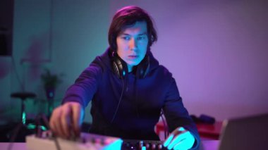 Ev kayıt stüdyosunda müzik çalan yakışıklı DJ portresi. Öğrenci yaratıcı atmosfer müziği yazmayı öğreniyor. Çevrimiçi eğitim. Ses çıkarıcı. Renkli Neon ışığı