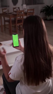 Ev soyutlanmış. Krom anahtar taşıyan esmer, yeşil ekran akıllı telefonun arkadaşıyla sohbet edişinin arka görüntüsü. Coronavirus Covid-19 uzaktan eğitim ya da çalışma konsepti karantinası. Dikey video