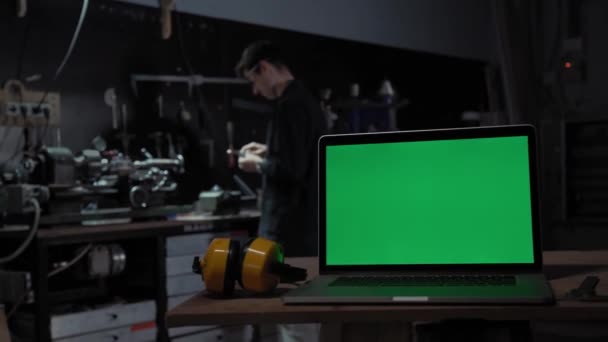 Laptop zöld képernyővel az ipari környezet hátterében. Egy munkás egy marógépnek dolgozik. A termelés és az építőipar fogalma