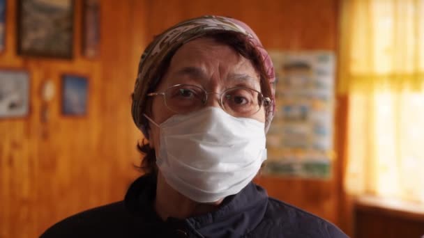 Ηλικιωμένη γυναίκα με μάσκα προστασίας στο σπίτι. Καραντίνα coronavirus covid-19 για τους ηλικιωμένους. Συνταξιοδότηση υγείας σε κίνδυνο, γιαγιά με μάσκα. COVID-19 πρόληψη πανδημία coronavirus. Κοινωνική — Αρχείο Βίντεο