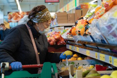 Koruyucu tıbbi maskeli yaşlı kadın markette limon seçiyor. Şehirdeki koronavirüs salgınının evde kalması gerekiyor. COVID-19 salgını. Sosyal uzaklık