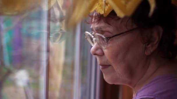 Hogar aislado. Una anciana mira por la ventana con tristeza. Brote de virus. Una anciana. COVID-19 prevención del coronavirus pandémico. Distanciamiento social — Vídeo de stock