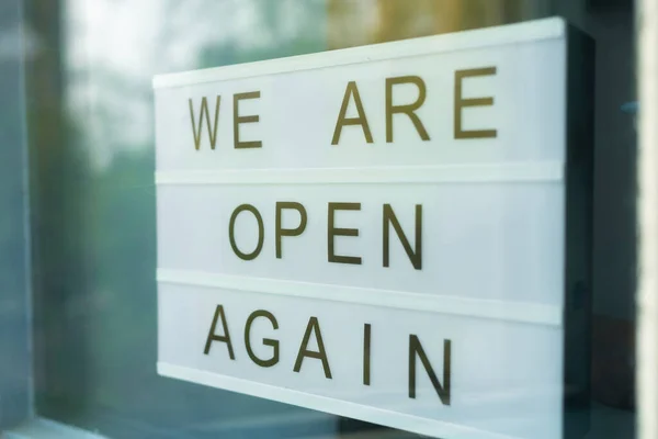 Lightbox with as sign we are open again behind a glass door of the cafe. Were open again after quarantine, video of small business owner. Please wear a face mask and keep your distance to protect — Stock Photo, Image