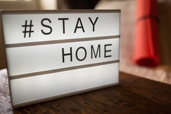 Coronavirus Yoga di home sign lightbox dengan tagar teks STAY HOME bersinar dalam cahaya dengan tikar olahraga, blok gabus. Panji COVID-19 untuk mempromosikan isolasi diri yang tinggal di rumah. Stok Lukisan  