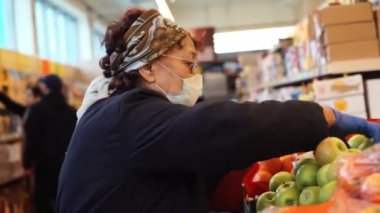 Ecza eldivenli yaşlı kadın süpermarkette seçim yapıyor. Şehirdeki koronavirüs salgınının evde kalması gerekiyor. COVID-19 salgını. Sosyal uzaklık