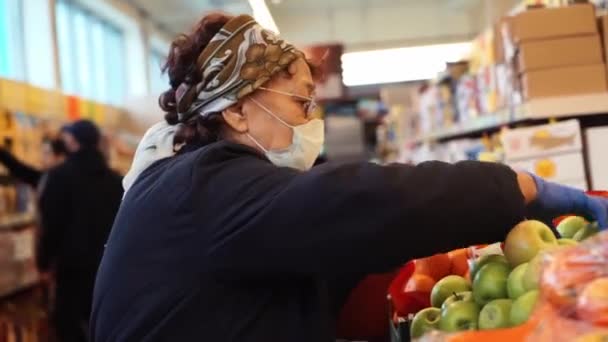 Пожилая женщина в медицинских перчатках выбирает в супермаркете. Эпидемия коронавируса в городе должна остаться дома. Пандемия COVID-19. Социальное дистанцирование — стоковое видео