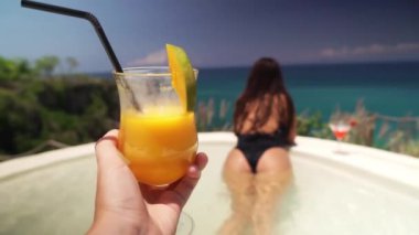 Bir adamın elinde turuncu bir İtalyan kokteyli tutarken çekilmiş bir fotoğrafı. Havuzda güzel bir kız var. Güzel bir yaz tatili konsepti.