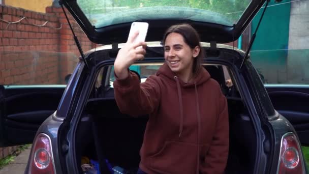 Zorgeloos opgewonden jonge vrouw nemen selfie shot op smartphone in stijlvolle kofferbak. Positief meisje poseren voor selfie, het maken van grappige gezicht en uitdrukkingen tijdens de zomer road trip — Stockvideo