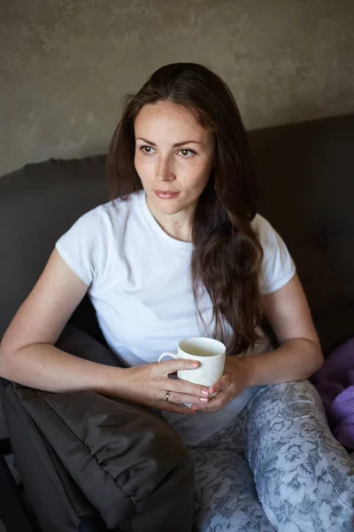 Woman sits on couch and drinking tea