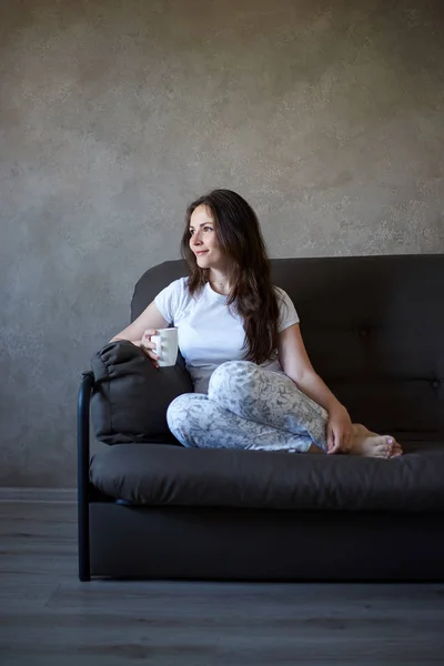 Woman sits on couch and drinking tea