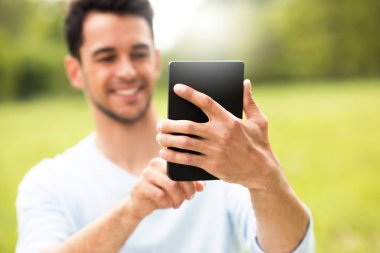 Genç güzel gülümseyen iş adamı doğa güneşli arka plan cihaz ile