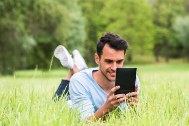 Gülümseyen iş adamı cihazını ile yeşil çim üzerinde yalan.
