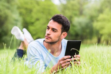 Düşünme ve aygıtla yeşil çim üzerinde yalan ciddi iş adamı.