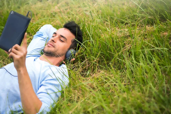 Молодий бізнесмен лежить на зеленій траві слухати музику, розслаблятися з пристроєм та навушниками — стокове фото