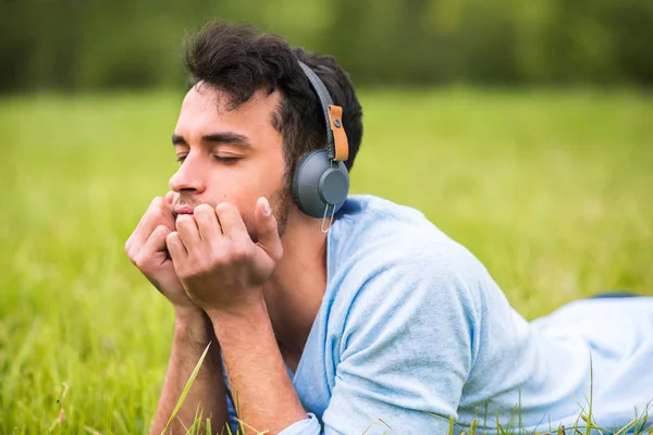 Красивий портрет молодого чоловіка, який насолоджується музикою з навушниками на зеленій траві, закриті очі — стокове фото