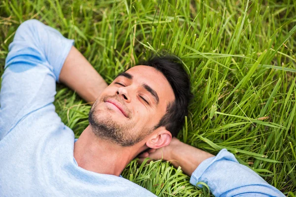 Handsome man on the green grass with his device look from back. — Stock Photo, Image