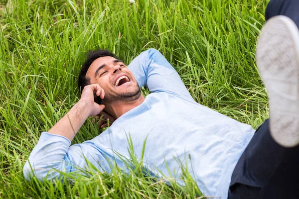 Щасливий розслабляючий бізнесмен лежить на зеленій траві з телефоном . — стокове фото