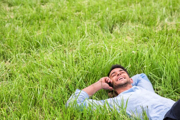 Щасливий мрійливий молодий бізнесмен лежить на зеленій траві. Розмова по телефону — стокове фото