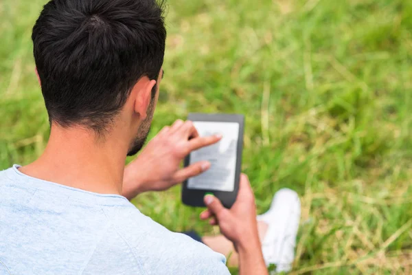 Mladý muž sedí v zelené trávě a používání tabletu za slunečného dne — Stock fotografie