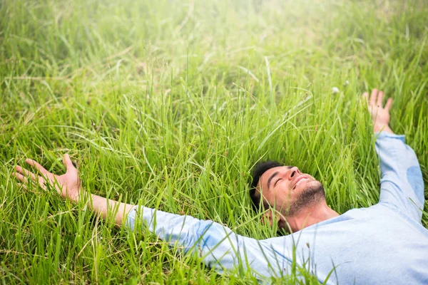 Handsome man on the green grass with his device look from back. — Stock Photo, Image