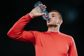 Portrét atraktivních mladých evropských sportovec pitné vody z láhve vzhlédl na sobě červené sportovní, relaxační, po spuštění nebo cvičení. Sportovní motivace. Životní styl.