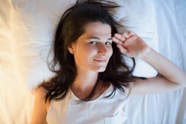 Beyaz yatakta güzel doğal genç kadın. Yukarıdan görüntülemek