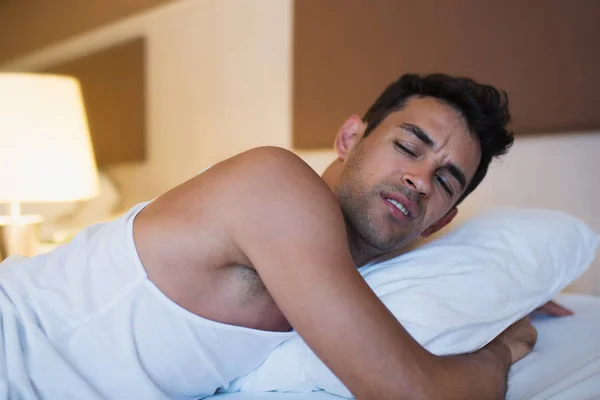 Retrato de un hombre infeliz sosteniendo una almohada en la cama blanca. Cama — Foto de Stock