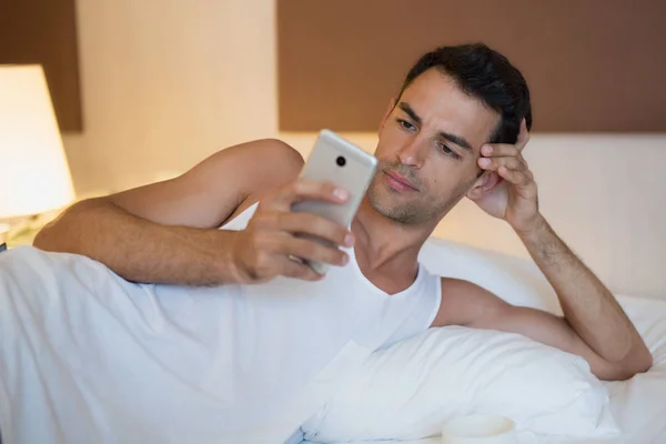 Hombre guapo usando un teléfono móvil en la cama blanca . — Foto de Stock