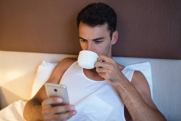 Portrait of handsome young man using a mobile phone and drinking — Stock Photo, Image