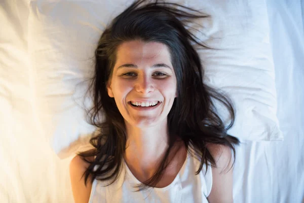 Engraçado sorrir jovem mulher na cama branca. Vista de cima — Fotografia de Stock