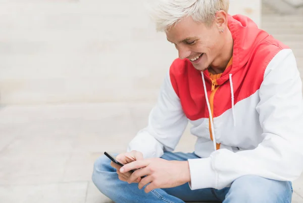 Side view of happy attractive young blond man smiling and textin