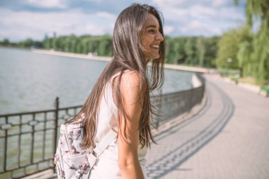 Park arka plan ile bir göl üzerinde rüzgarlı bir uzun saçlı güzel gülümseme ile mutlu genç esmer kadın portresi. Bir tarafa bakıyor. Seyahat.