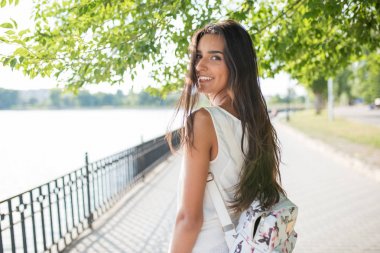 Arkasında göl üzerinde arka plan, doğa arka plan bakmak güzel portre gülümseyen genç esmer kadın sırt çantası ile. Parkta üzerinde yürüme. Seyahat. Tatil