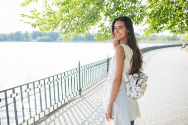Arka taraftan göl ile parkta yürüyüş seyir sırt çantası, genç kadınla gülümseyerek. Seyahat. Tatil
